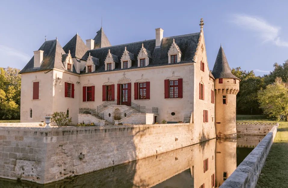 Château Olivier, a Renaissance-style castle with white stone facade and slate roofs, surrounded by a water-filled moat, located in the Bordeaux region