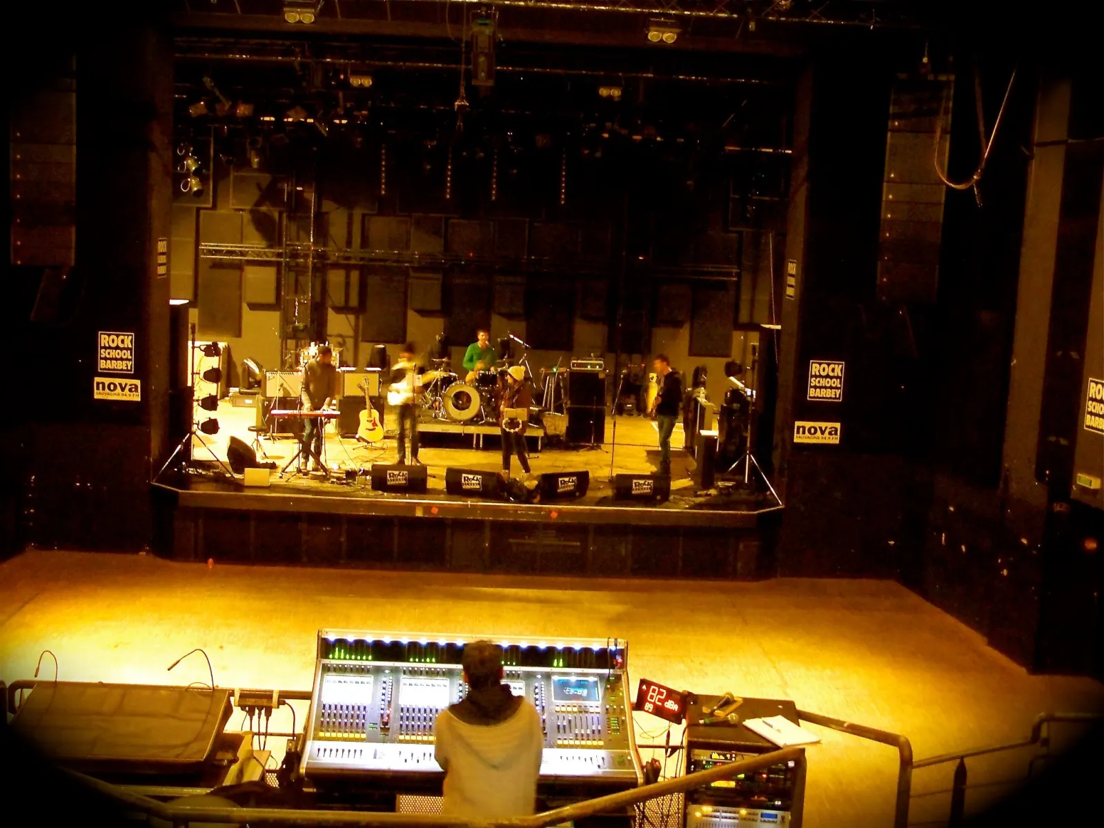 Stage view of Rock School Barbey in Bordeaux showing musicians performing, controlled by a sound engineer at the mixing console in the foreground.