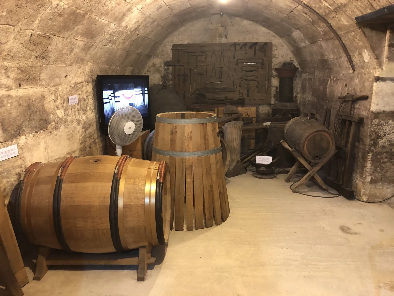 Vaulted cellar interior at the Bordeaux Wine and Trading Museum displaying wooden barrels, casks, and traditional winemaking equipment with an information screen.