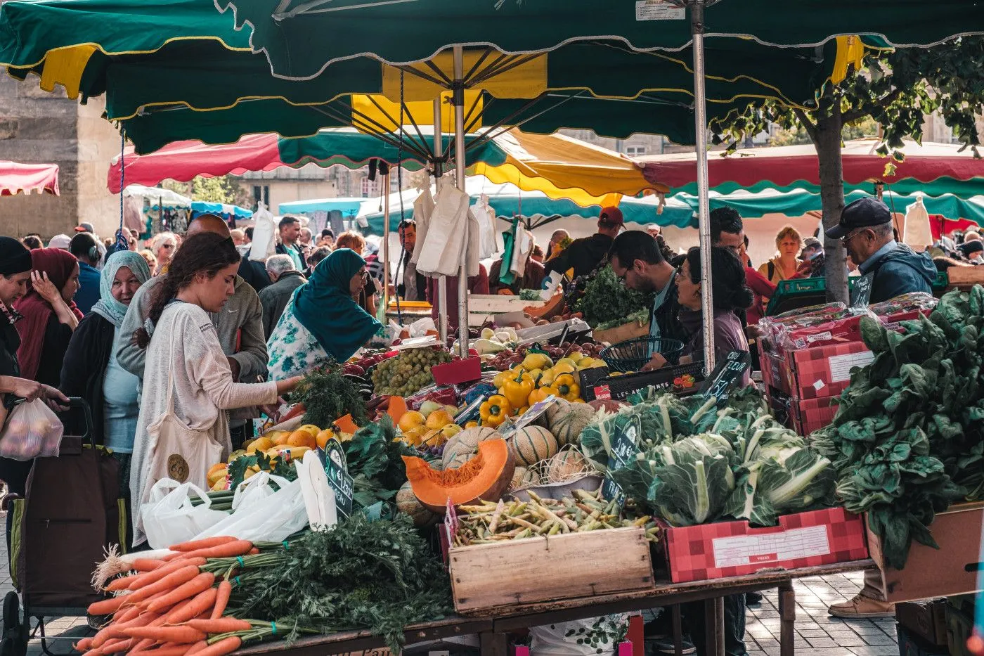 Open-air market in Bordeaux with fresh produce stalls under green and yellow awnings, shoppers browsing between vendors' stands