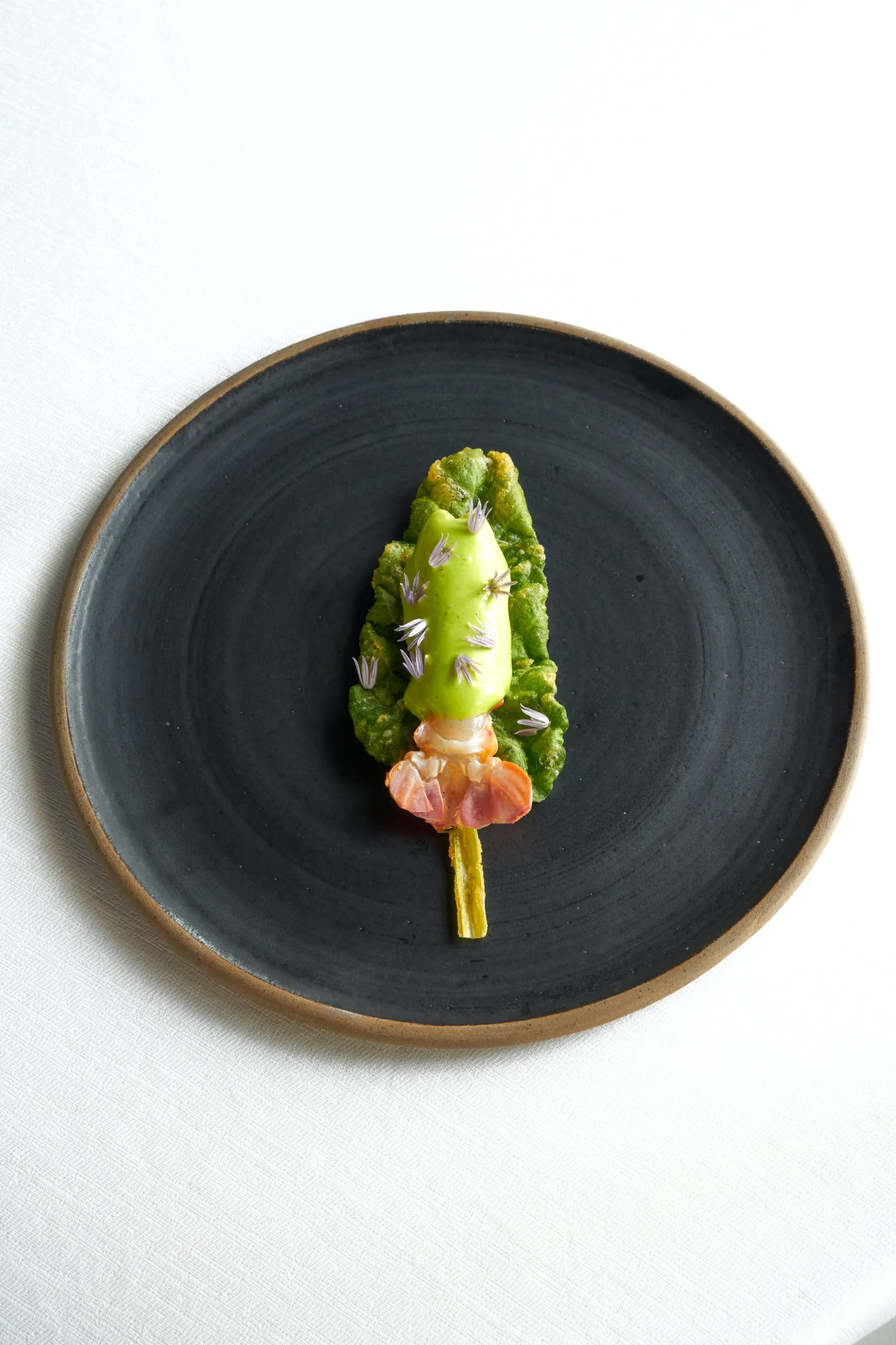 Black plate featuring a gourmet dish with green romaine lettuce, smoked salmon, and microgreens artistically plated at La Grand'Vigne restaurant in Bordeaux.
