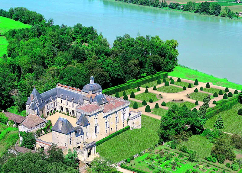 Aerial view of Château de Vayres near Bordeaux, a stone historic mansion with slate roofs overlooking the Dordogne river, surrounded by manicured gardens and lush greenery.