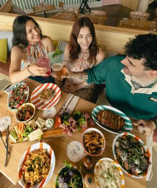 Three smiling people seated at a restaurant table in Bordeaux, enjoying various dishes and drinks with multiple shared small plates spread across the table.