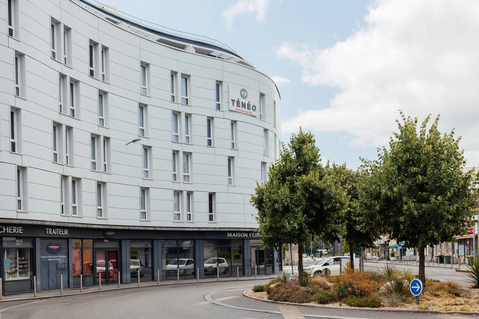 Ténéo Aparthotel building in Talence, Bordeaux, featuring modern white architecture with regular windows, ground floor shops, and landscaped trees.