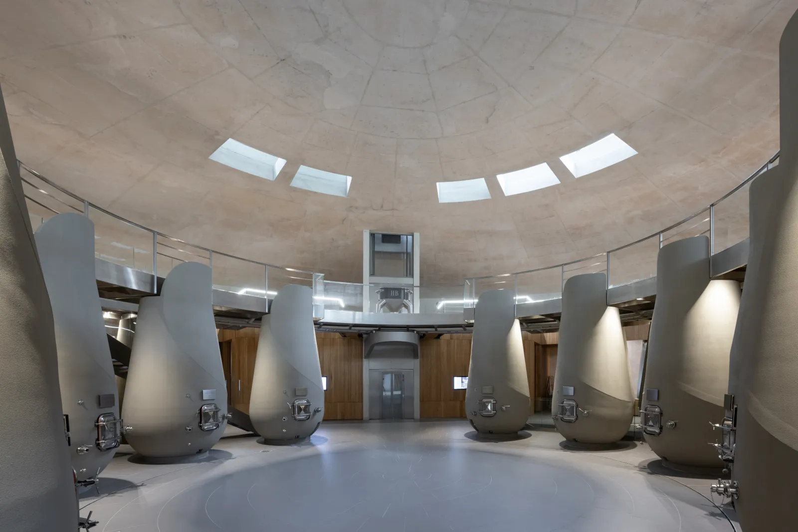 Interior of a circular winemaking cellar featuring concrete fermentation tanks, domed ceiling with skylights, glass railings and wooden doors at Château Haut-Bailly in Bordeaux.