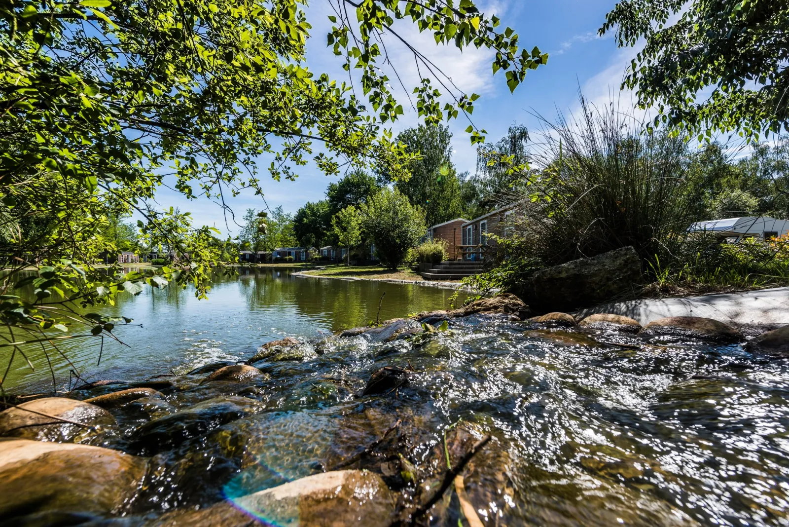 Scenic stream with rocks in the foreground, surrounded by lush greenery and a brick house near Bordeaux Lake, Yelloh! Village.