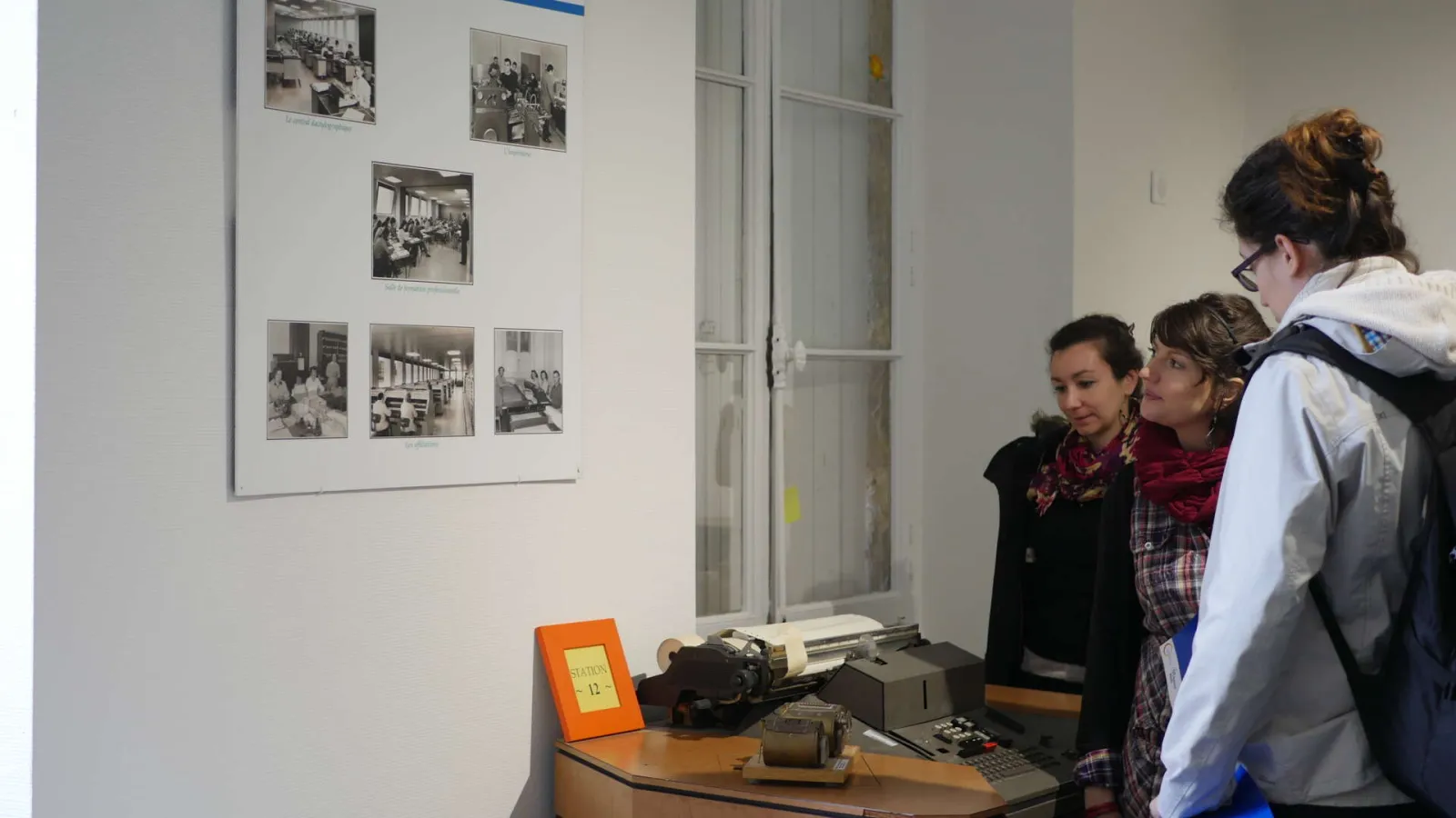 Three visitors examine historical medical equipment displayed in a case at the National Health Insurance Museum in Bordeaux, with black and white photographs mounted on the wall.