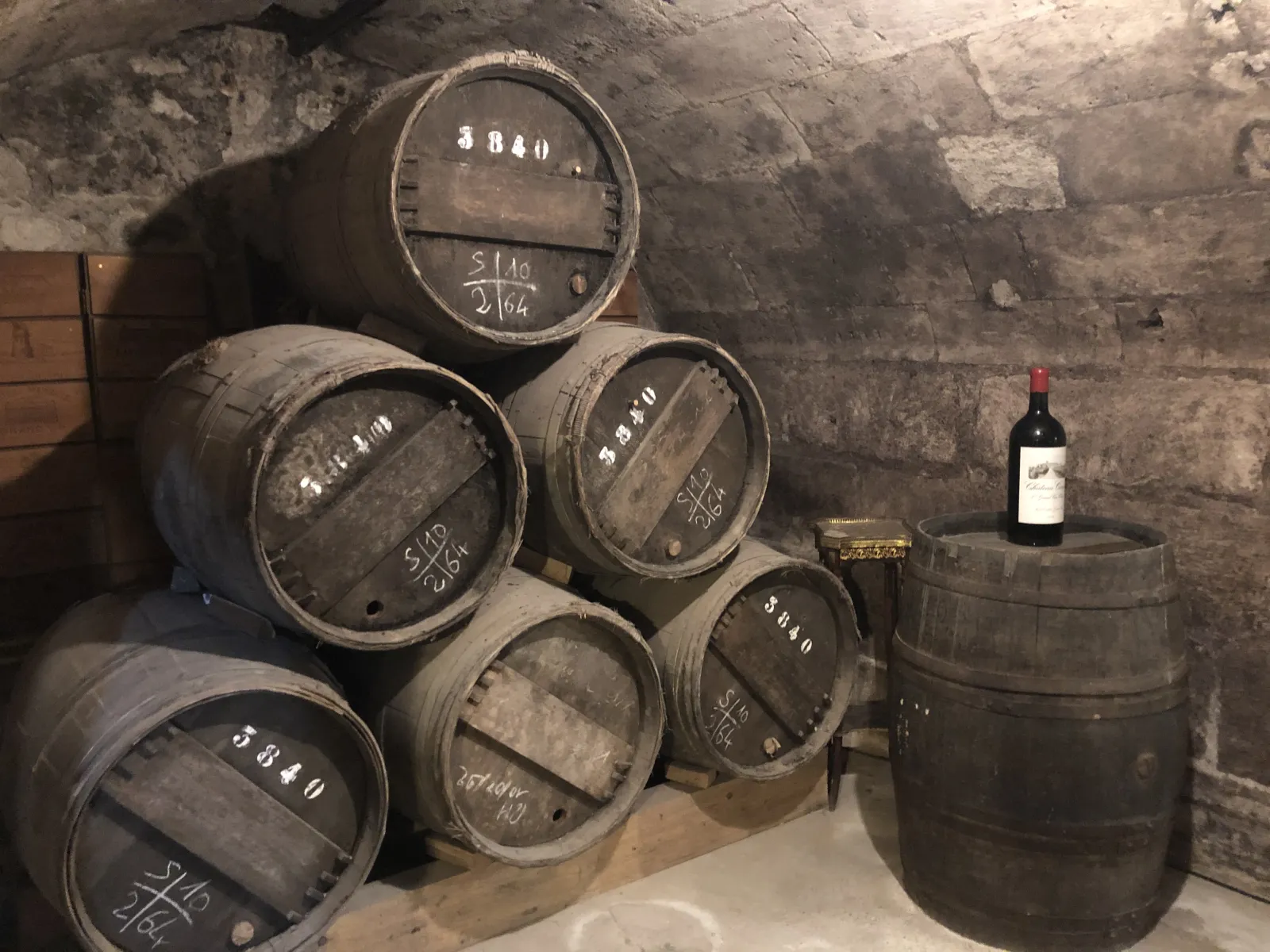Wine barrels stored in a stone vaulted cellar at the Wine and Trade Museum in Bordeaux, with a wine bottle displayed on a barrel to the right
