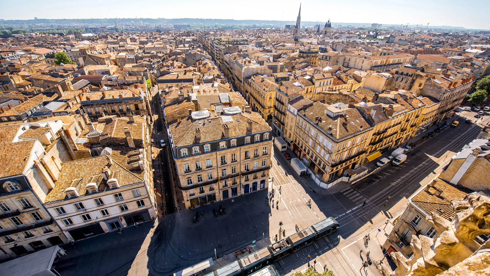 Aerial view of Bordeaux from Pey-Berland Tower showing ochre-colored rooftops of Haussmann buildings, paved streets, and the urban skyline with the cathedral in the background