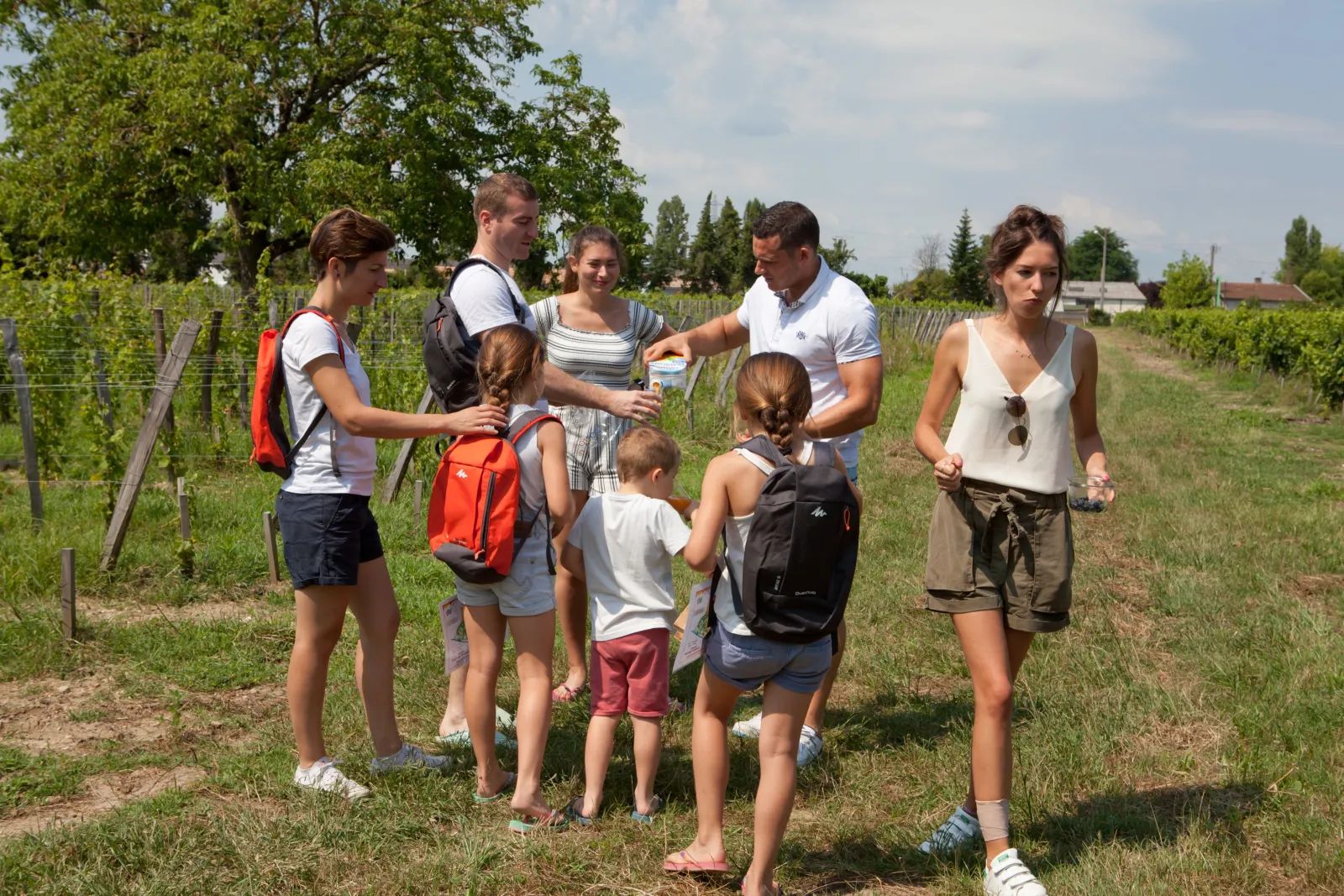 A group of adults and children gathered in a vineyard during an educational guided tour, with rows of vines in the background.