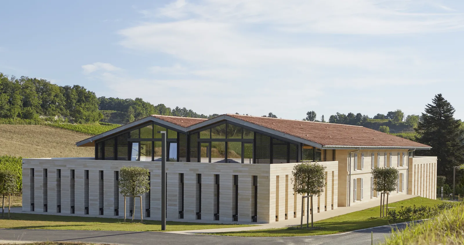 Château Peby Faugères in Bordeaux: modern architectural building with white and grey facades, red tile roof, large glass panels and black shutters, surrounded by landscaped gardens and vineyards.
