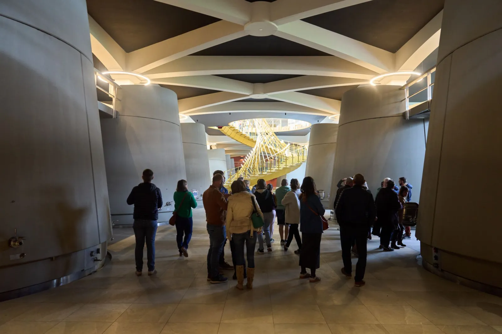 Group of visitors in a modern hall at Château Pichon Longueville in Bordeaux, featuring geometric ceiling lighting and a golden staircase in the background
