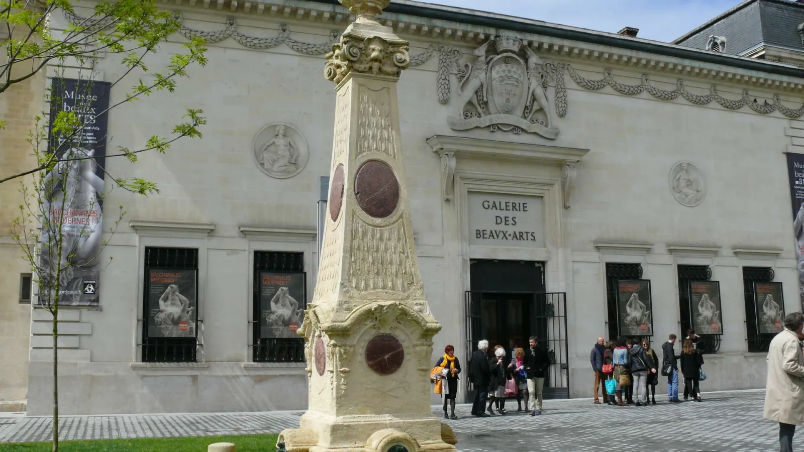 Facade of the Bordeaux Museum of Fine Arts with a stone commemorative monument in the foreground and visitors at the main entrance