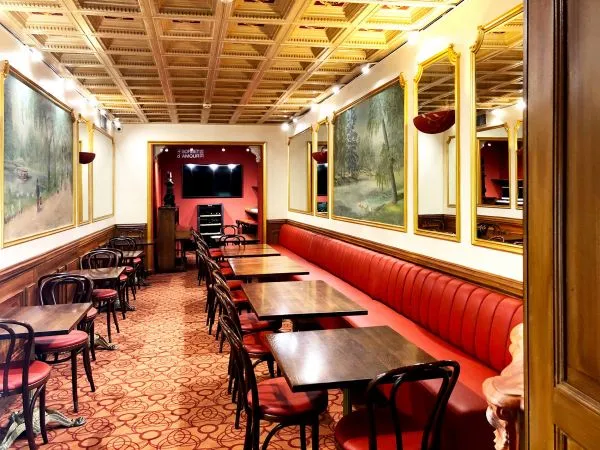 Elegant interior of QuatrèS Café in Bordeaux featuring red banquette seating, black chairs, wall paintings, coffered golden ceiling, and bar area