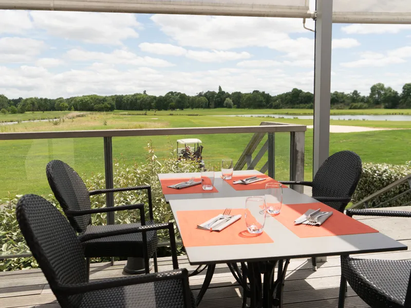 Terrace of Le Club restaurant with an orange and black set table, overlooking the lush fairways of Golf du Pian Médoc near Bordeaux