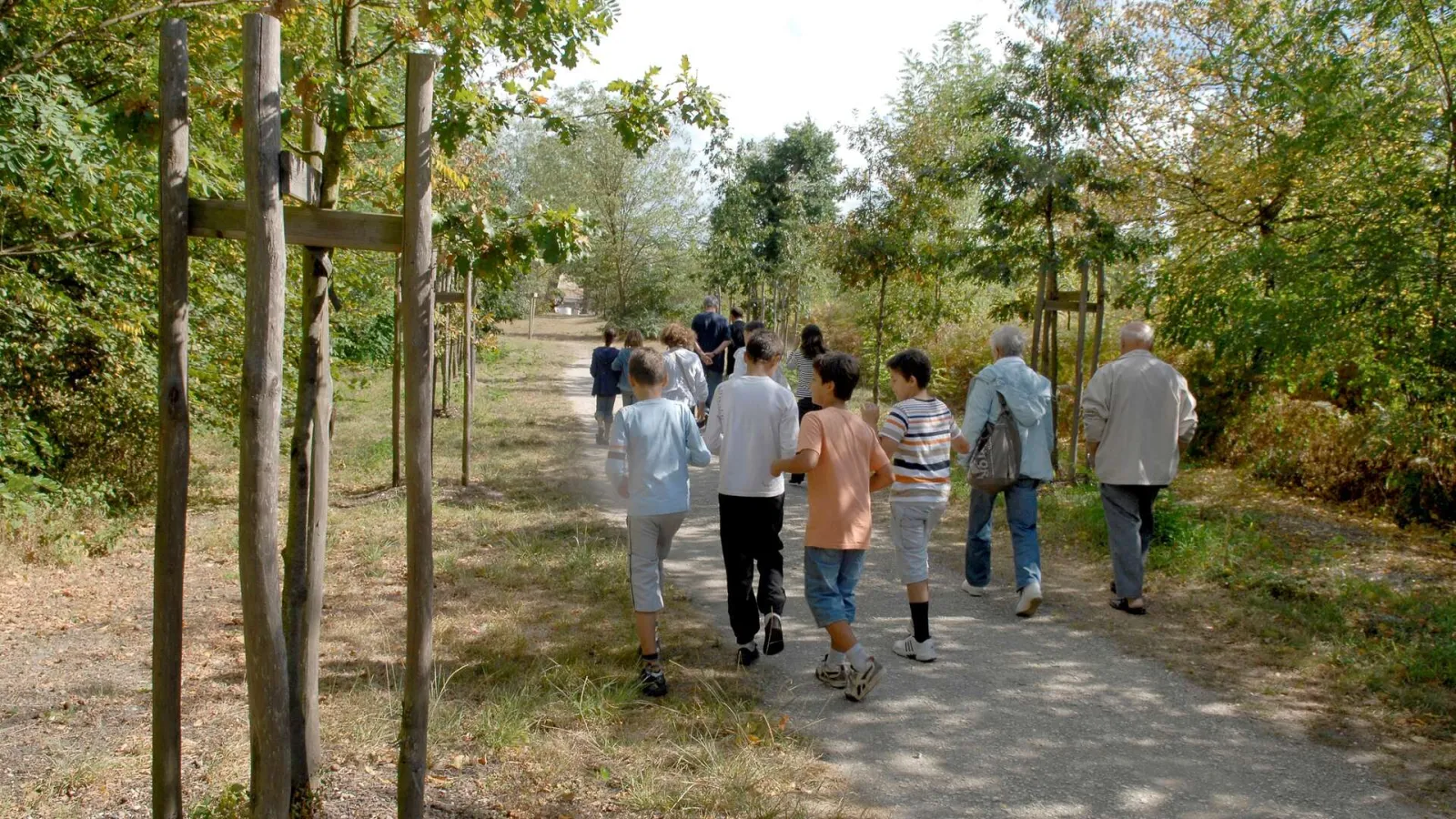 A diverse group of people of all ages jogging together on a shaded trail in the Bois de Thouars in Bordeaux, surrounded by trees and greenery.