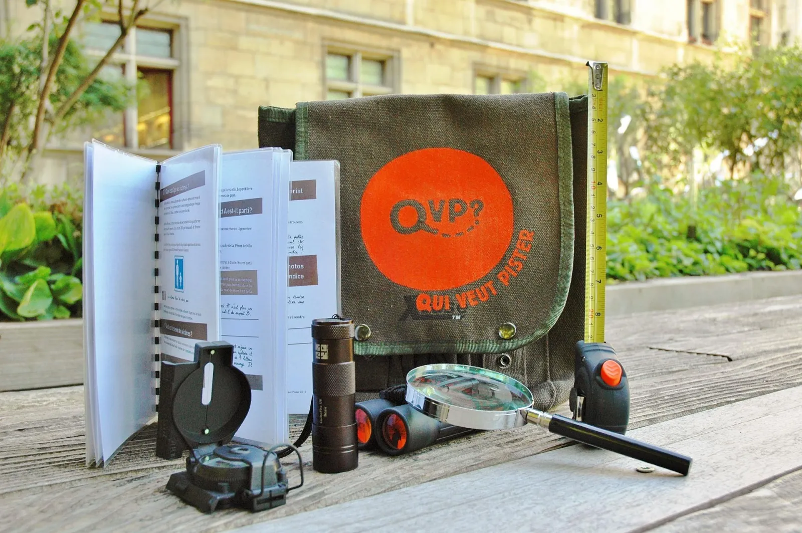 Treasure hunt kit 'Who wants to track Bordeaux' featuring backpack, notebook, compass, flashlight, measuring tape and exploration tools on a Bordeaux terrace