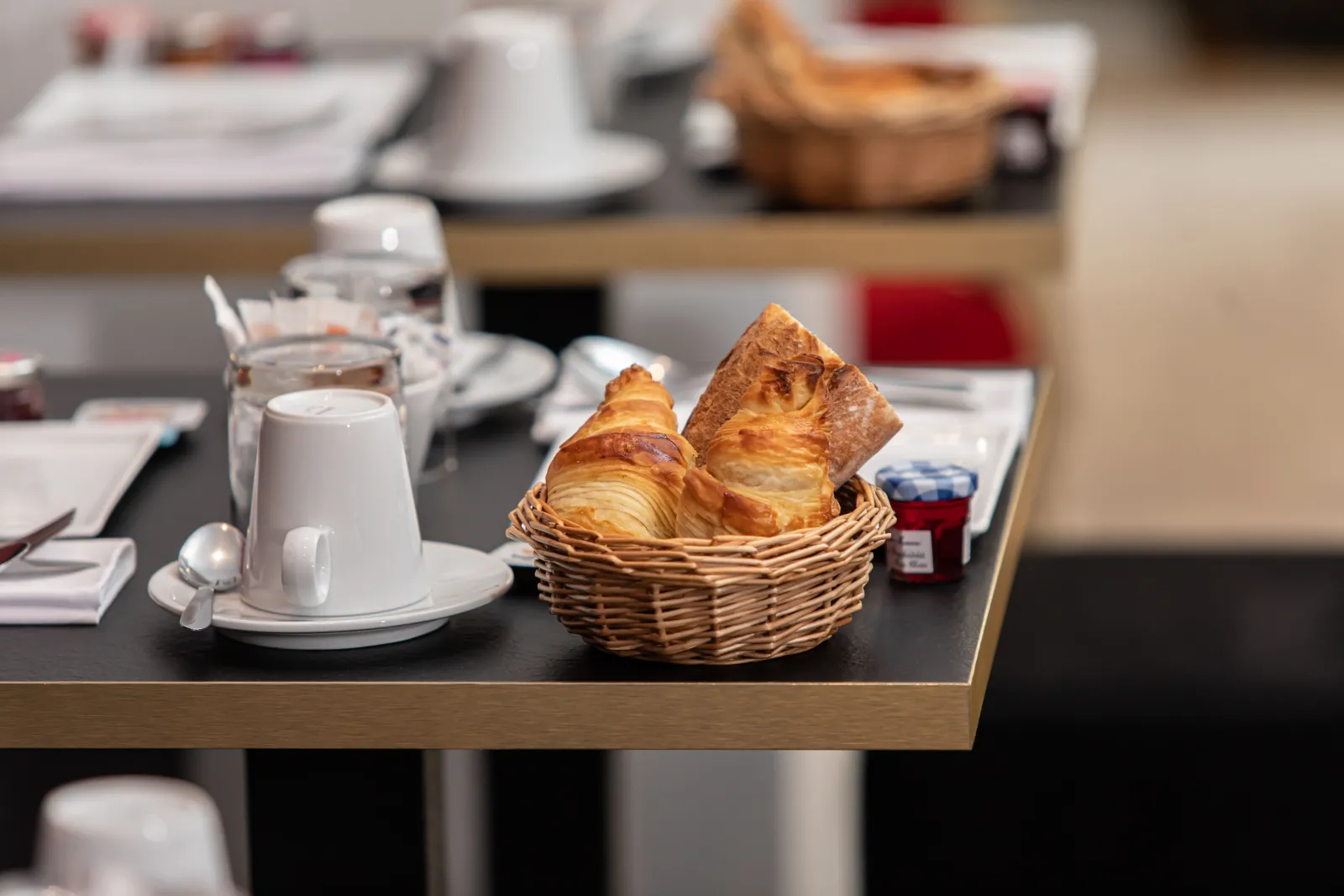 Breakfast table at Hotel Churchill in Bordeaux featuring a basket of fresh croissants, white coffee cup, water glass, and elegant table settings