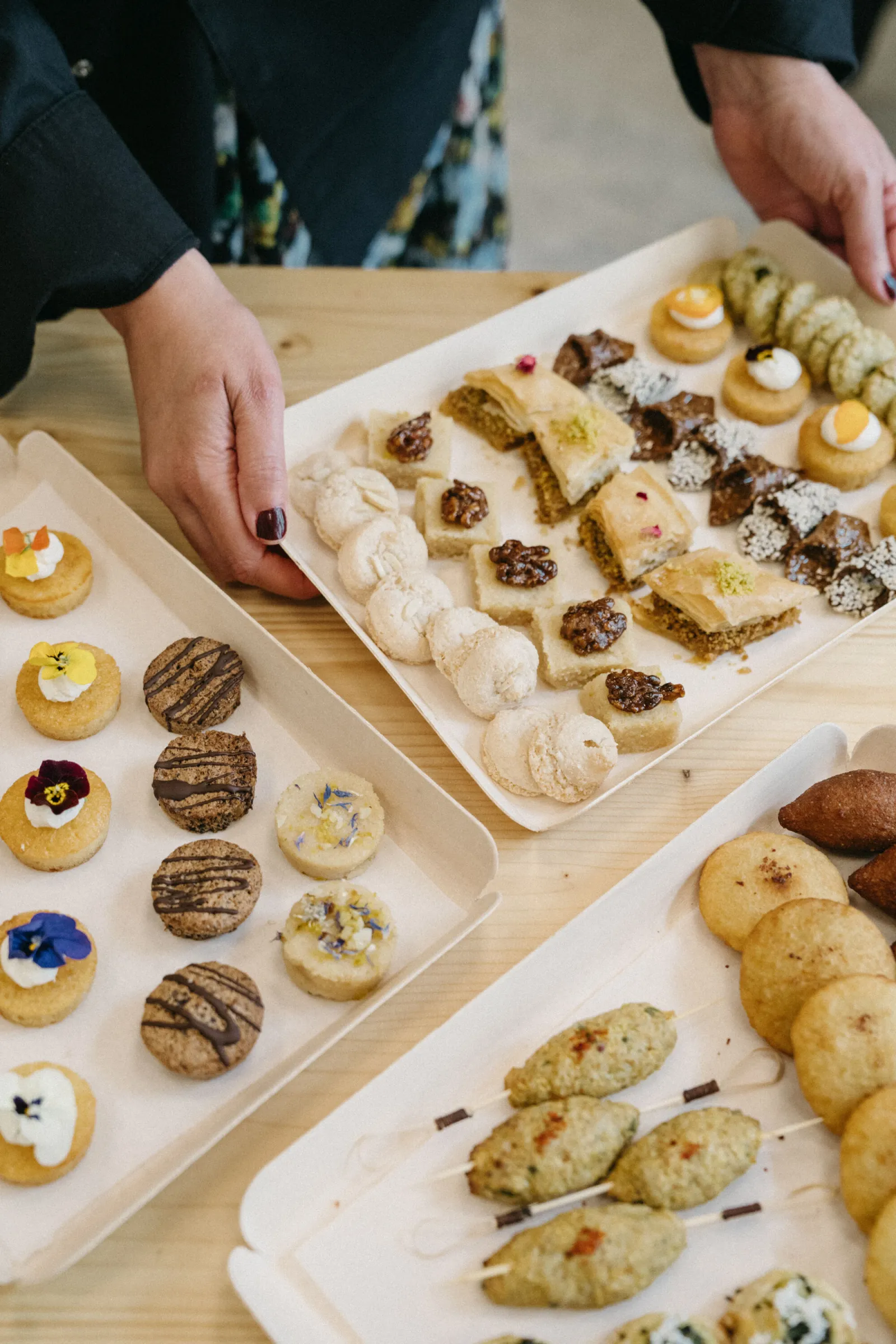 Display of various handcrafted pastries and cookies including macarons, financiers, decorated shortbreads and petit fours arranged on white plates in a restaurant setting.