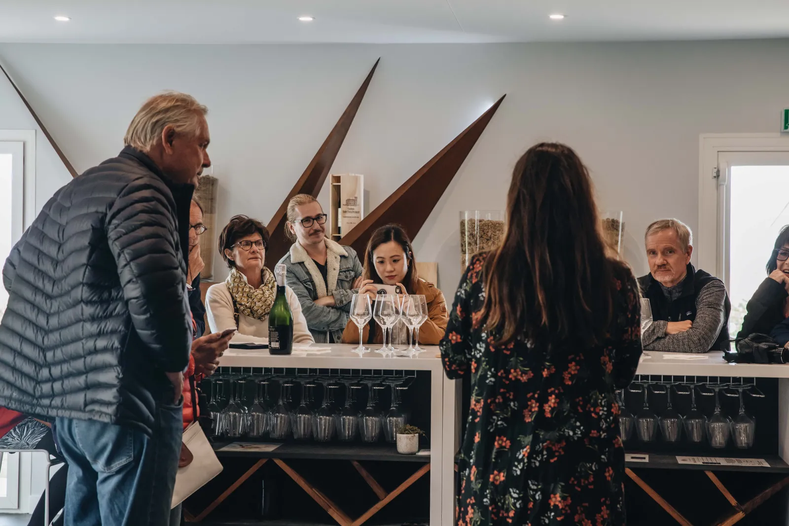 Visitors listening to a wine tasting presentation at Château Ambe Tour Pourret in Bordeaux, with wine glasses and a bottle displayed on the counter.