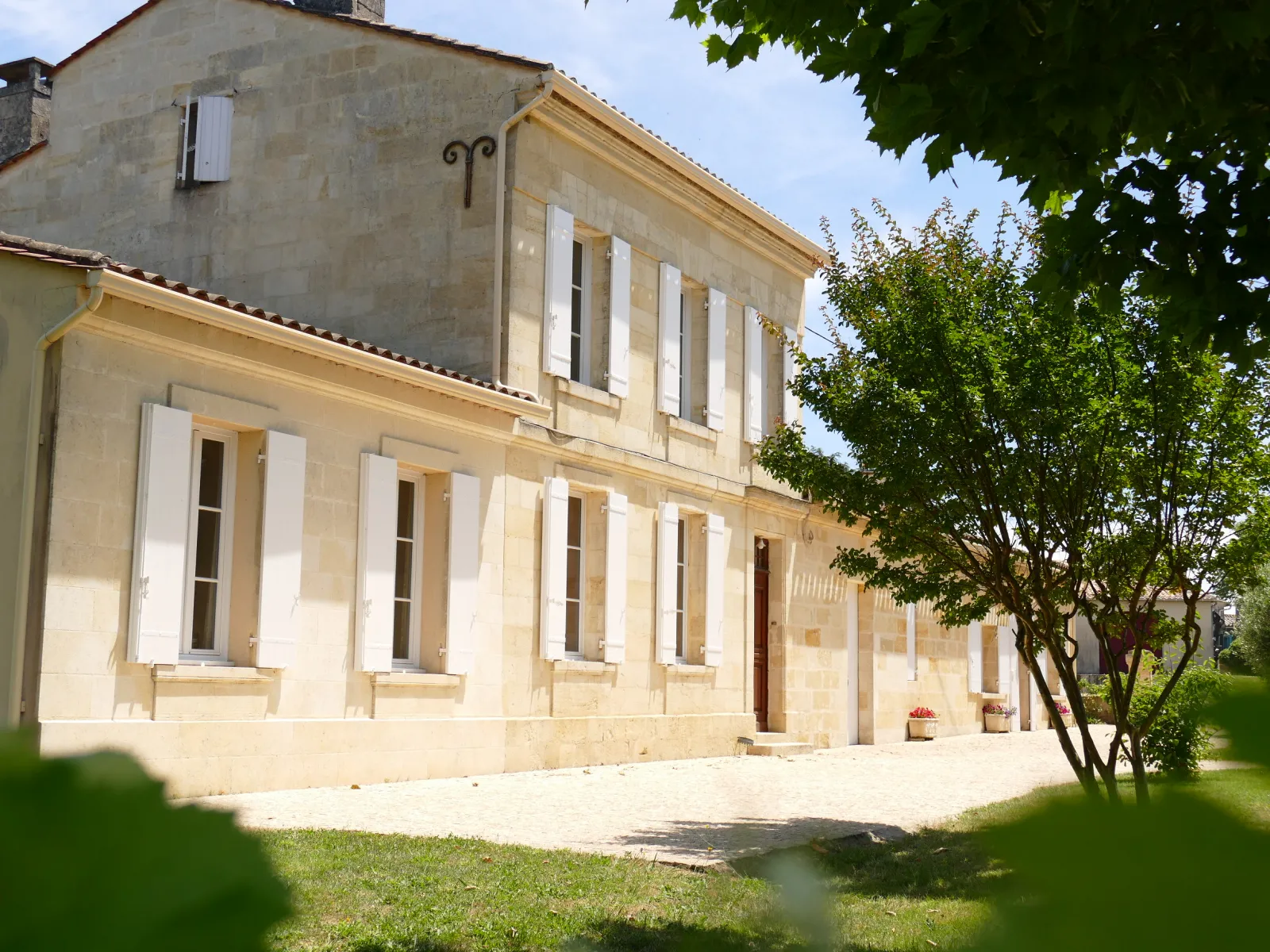 Facade of Château Laniote in Bordeaux, a classical stone building with white shutters, regularly spaced windows and landscaped surroundings