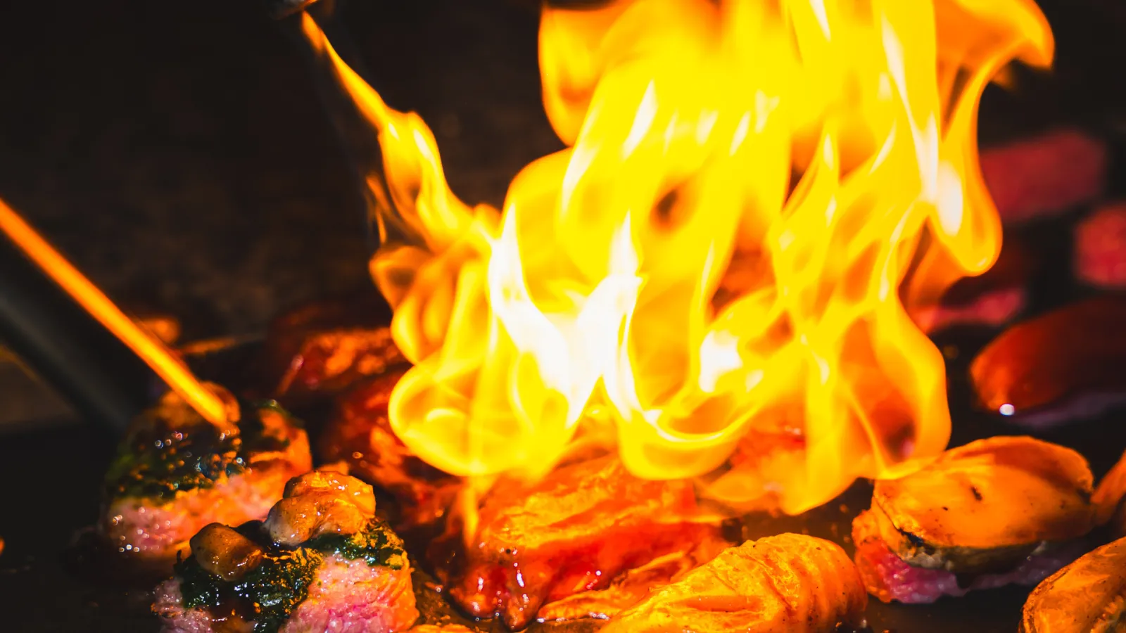 Bright yellow and orange flames rising above glowing embers and hot coals in a fire pit
