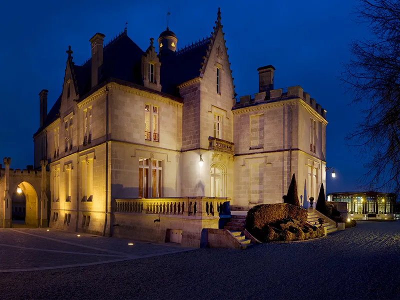 Illuminated château at night in Bordeaux, neoclassical architecture with towers and stone facade, golden lighting highlighting architectural details.