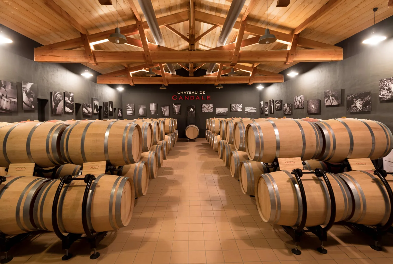 Barrel aging cellar at Château de Candale in Bordeaux featuring rows of oak barrels under modern architecture with exposed wooden beams.
