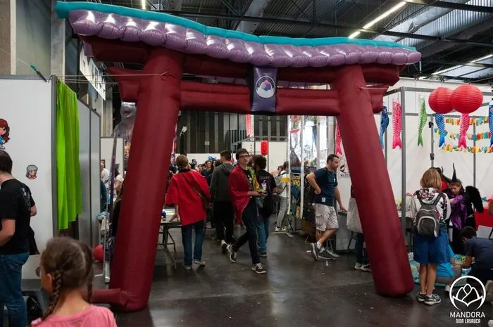 Red torii gate entrance at Bordeaux's Animasia festival, with visitors walking beneath the decorated structure adorned with lanterns in an exhibition hall.