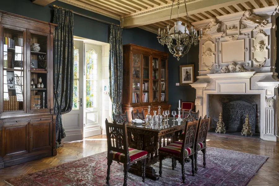 Elegant dining room of Château Toulouse-Lautrec in Bordeaux, featuring a wooden table, richly decorated chairs, ornate white fireplace, period furniture, and bronze chandelier with classical refined décor.