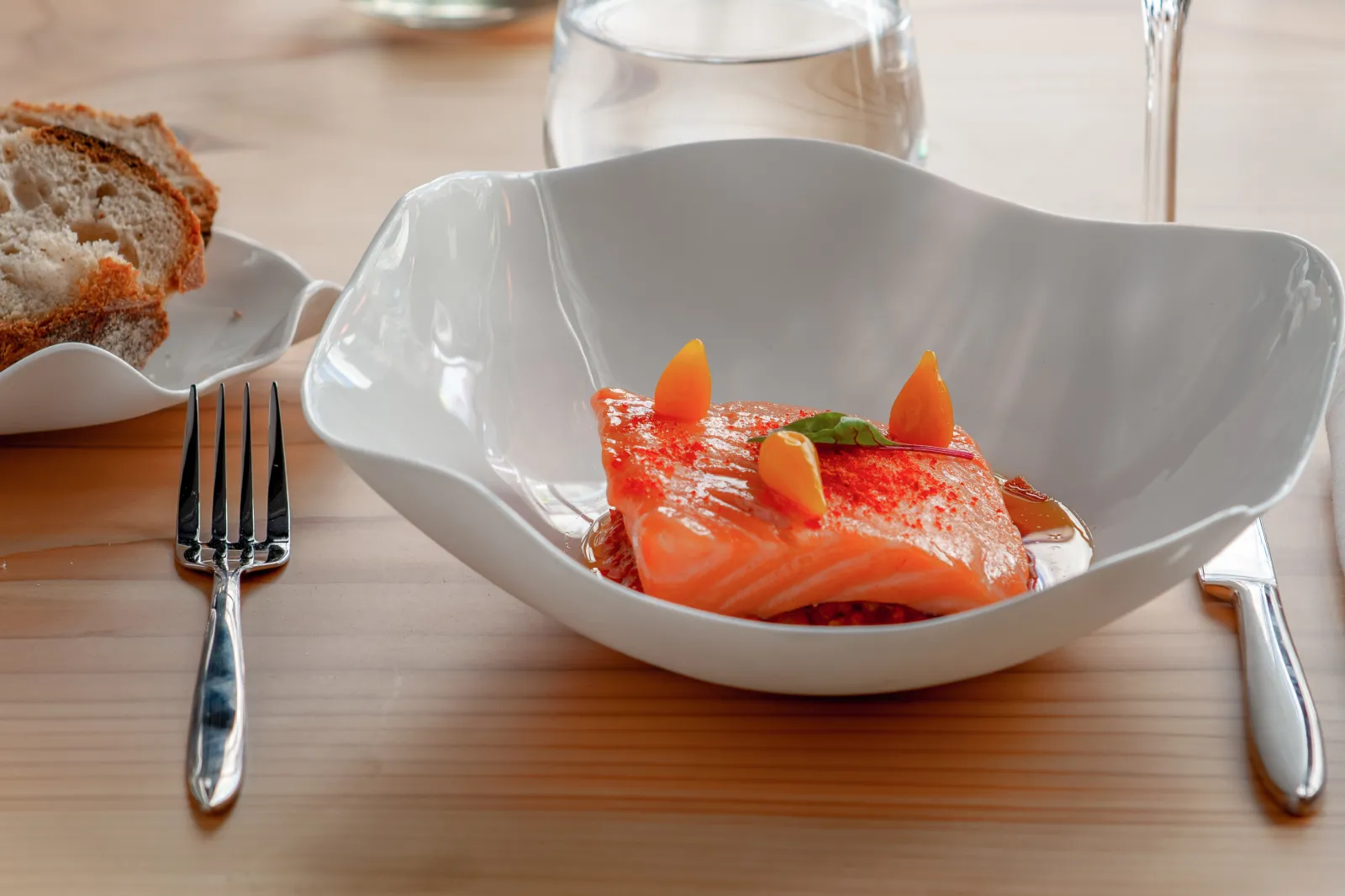 Elegantly plated salmon with red glaze and colorful garnishes, served with toasted bread and a glass of water, at restaurant le Loup in Bordeaux