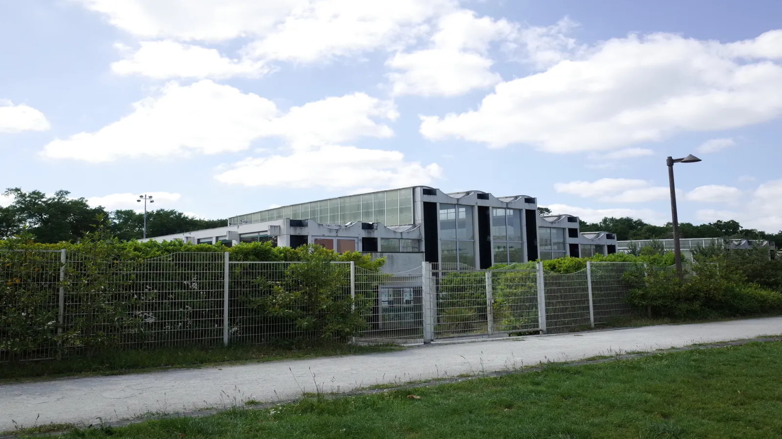 Exterior view of Henri Deschamps Aquatic Stadium in Bordeaux featuring modern glass and steel buildings surrounded by metal fencing and greenery