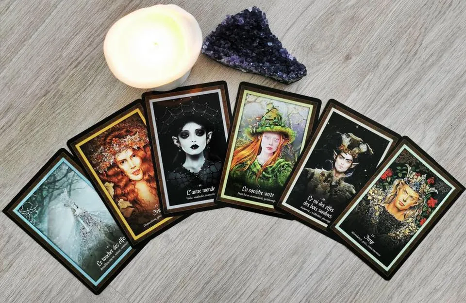 Tarot cards arranged in a fan layout with French inscriptions, accompanied by a lit white candle and purple amethyst crystal on gray wooden surface.