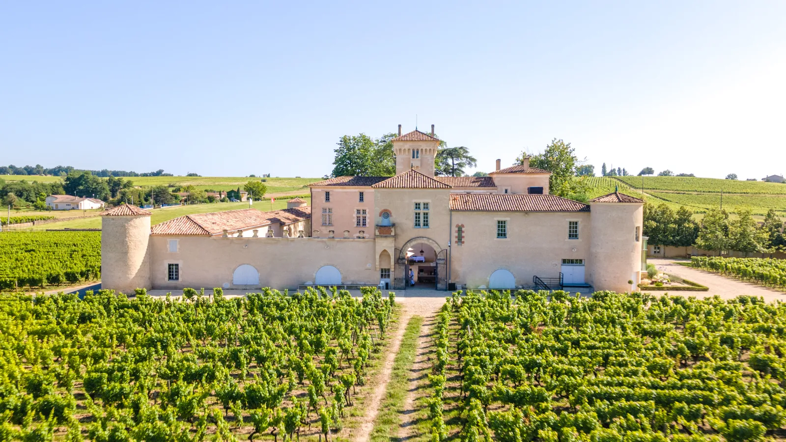 Lafaurie-Peyraguey Castle, a historic pink-walled estate with central tower and red-tiled roof, surrounded by lush vineyards in the Bordeaux region.