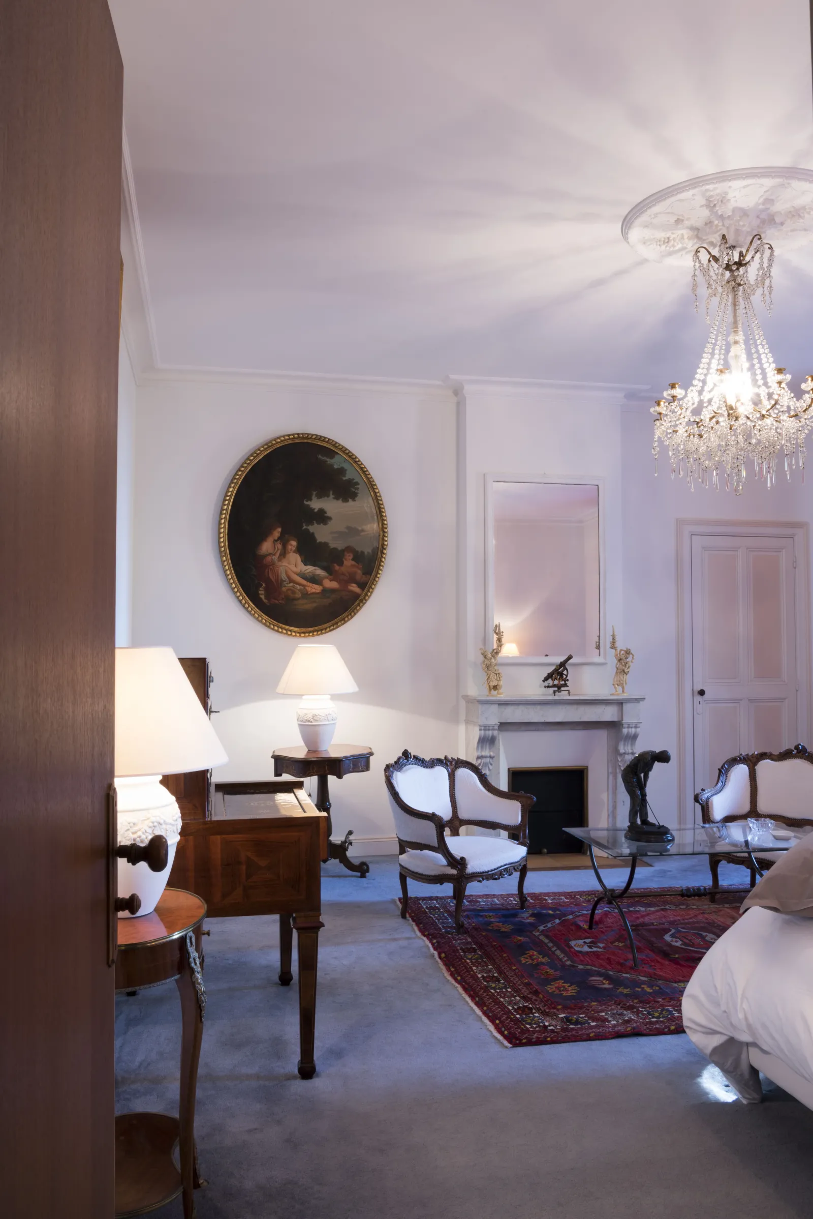 Elegant living room at Château Bellefont-Belcier in Bordeaux featuring period furniture, crystal chandelier, fireplace, ornate portrait and Oriental rug on blue parquet floor.