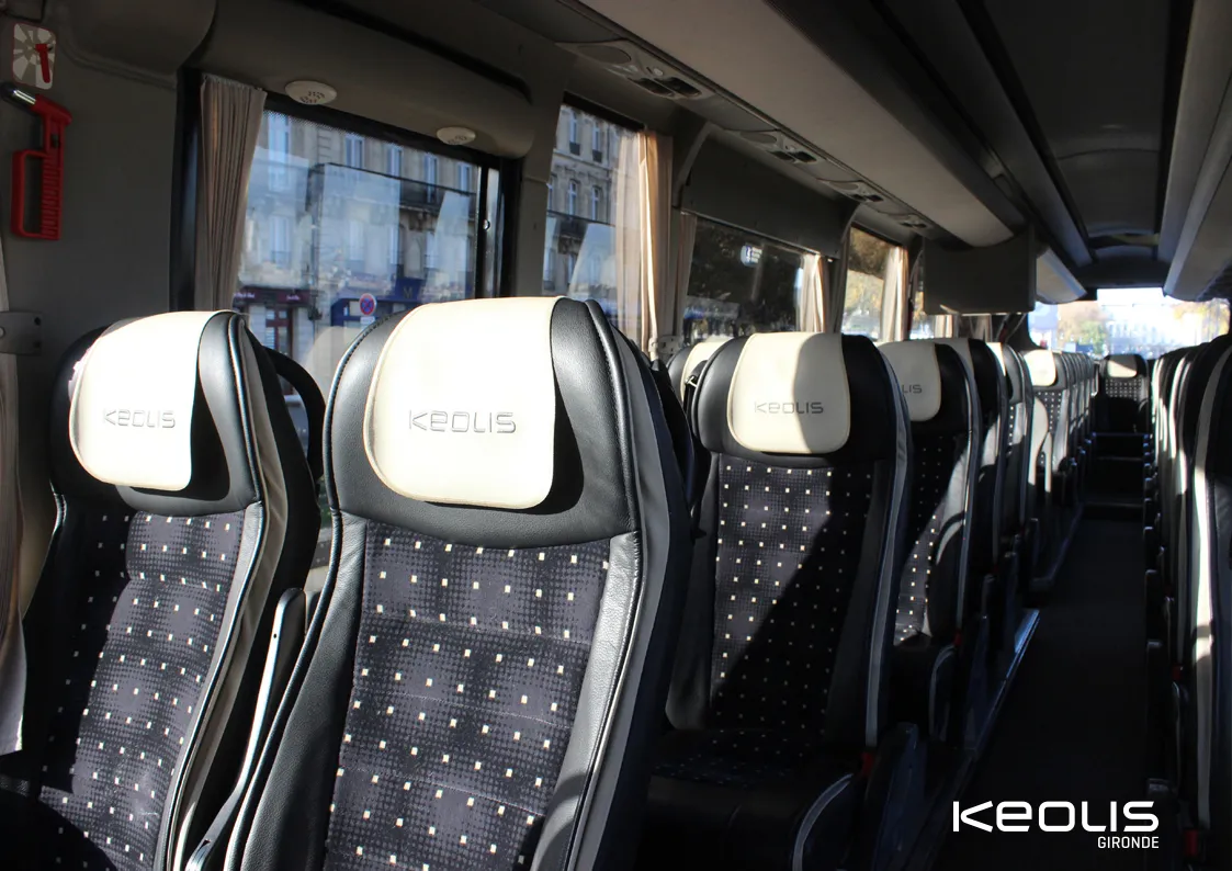 Interior of a Keolis Gironde coach bus in Bordeaux featuring black and white seats in a row, windows with curtains and city view.