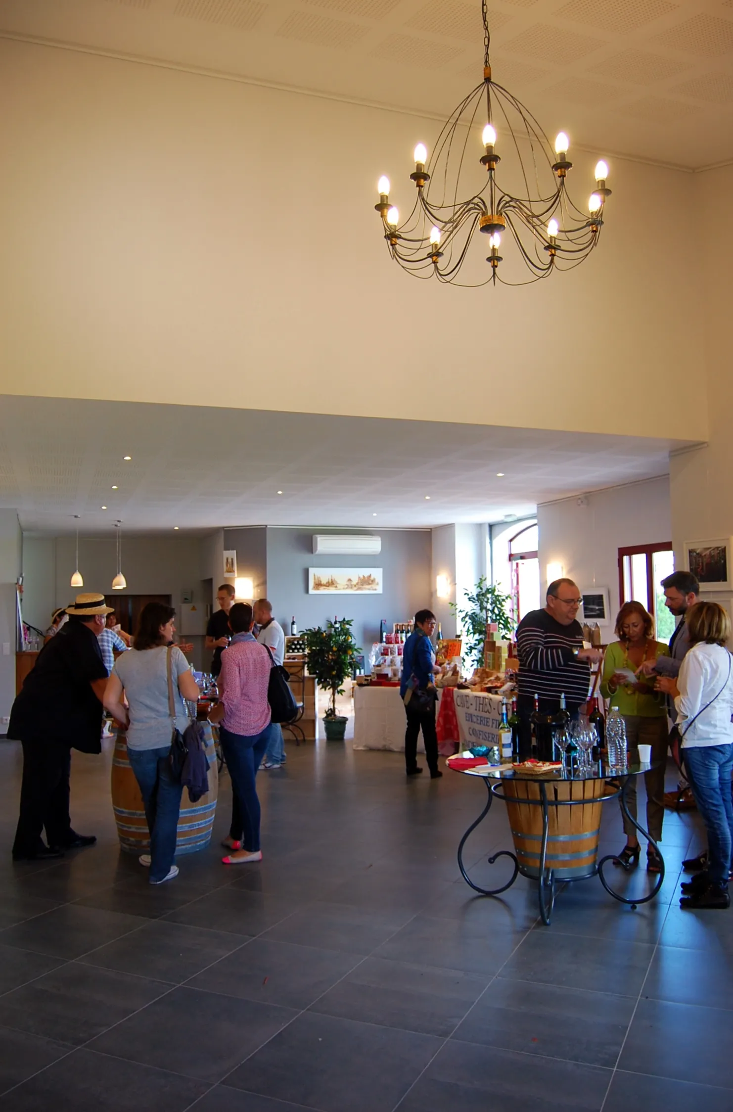 Spacious interior of Château Pichon Bellevue in Bordeaux with visitors gathered in a modern hall, an elegant chandelier overhead, and a tasting counter.