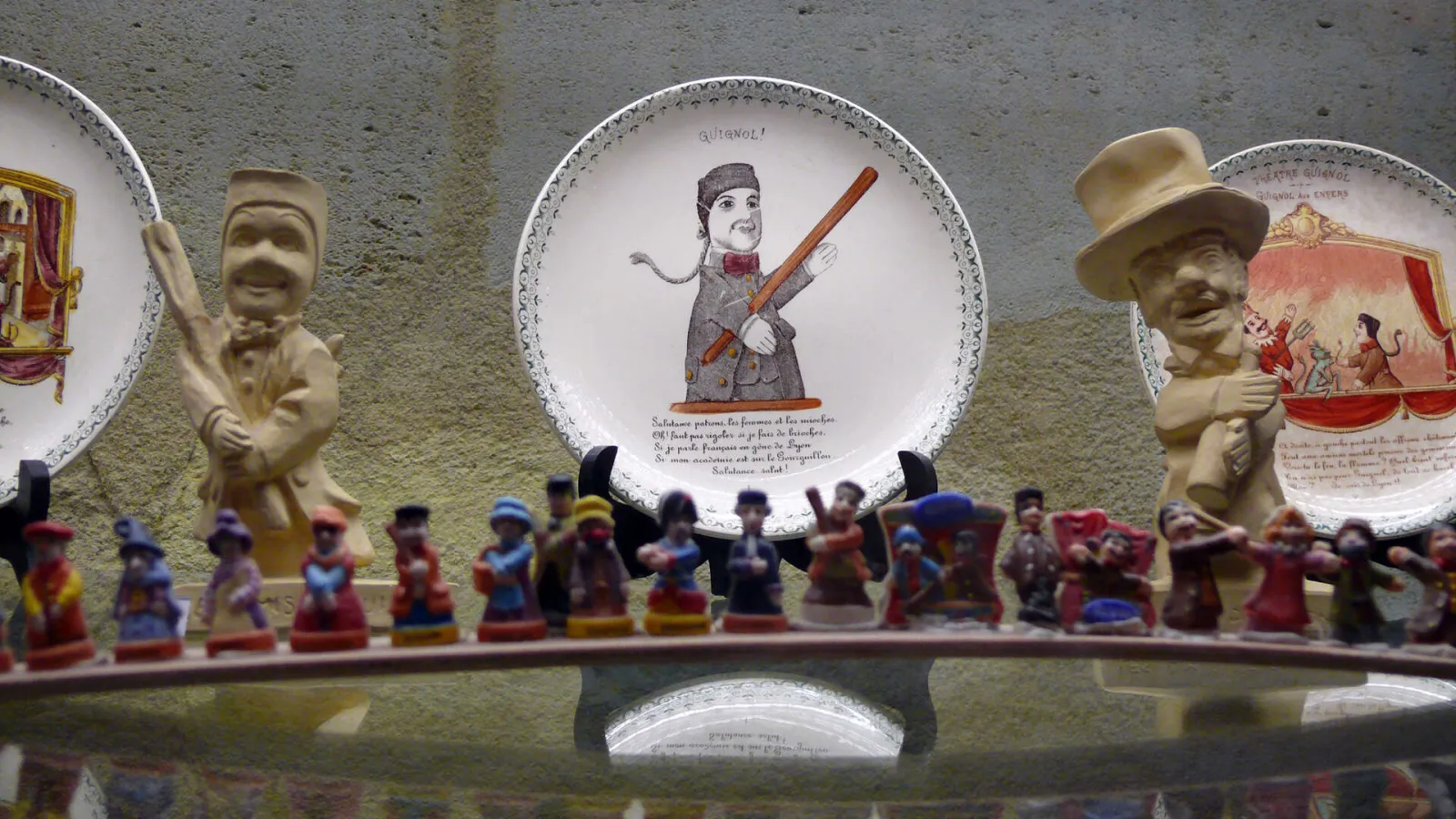 Display case at the Guignol Guérin Theater in Bordeaux featuring colorful puppet figurines arranged on a platform, with decorative historical plates and terracotta busts in the background.