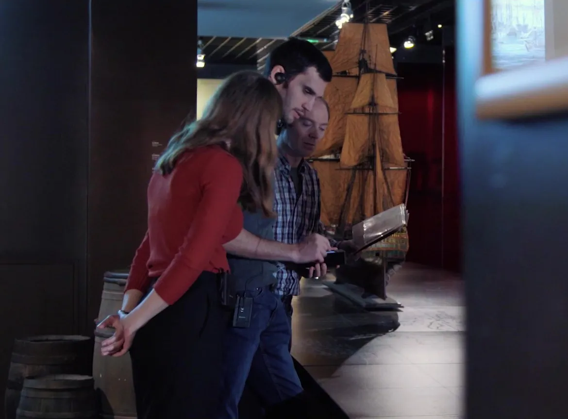 Three visitors examining a historical ship model at the Musée d'Aquitaine, with one person holding an informational document.