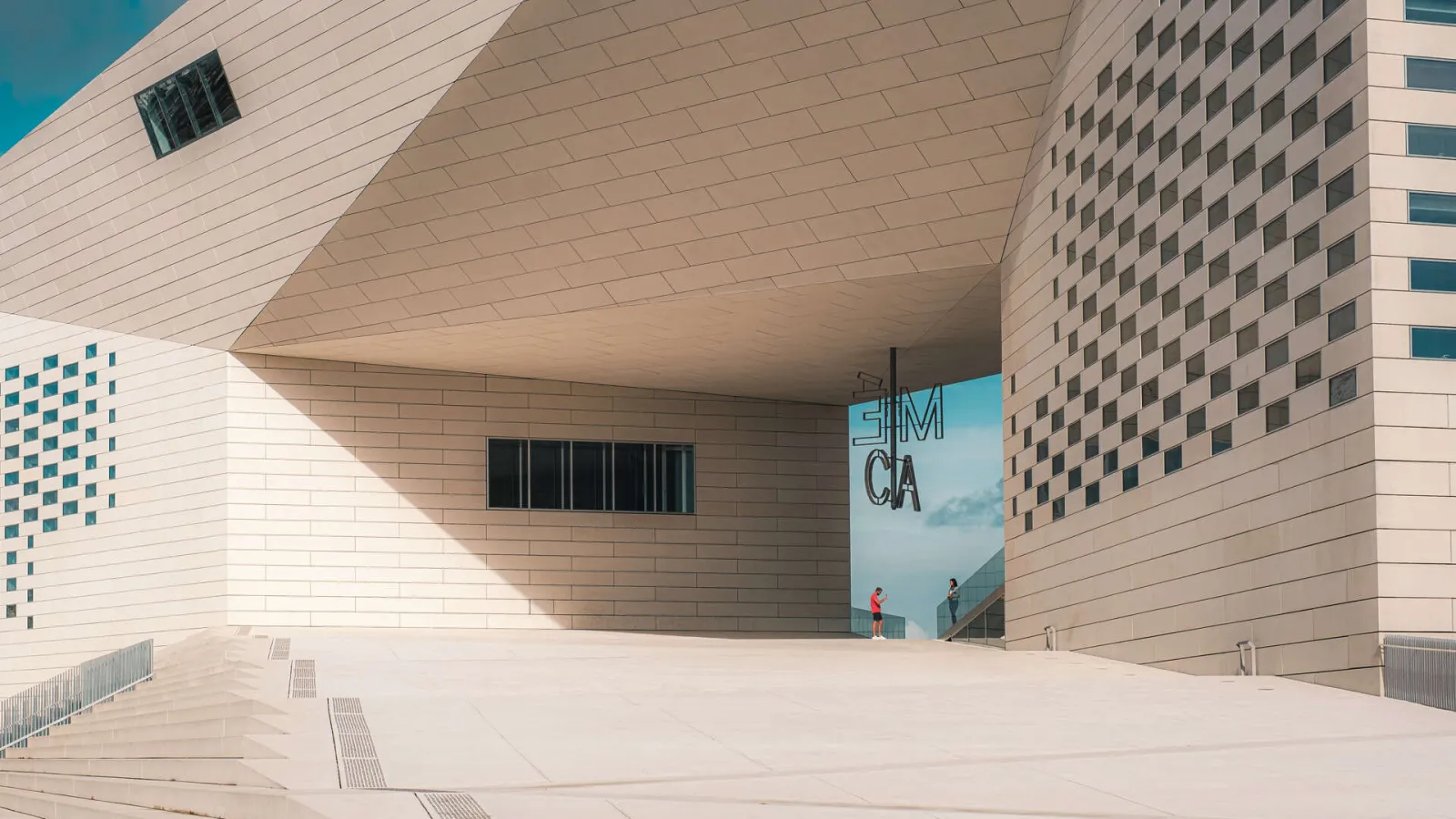 La Méca in Bordeaux, modern building with light stone façade, spacious entrance with stairs and blue signage, under clear sky.