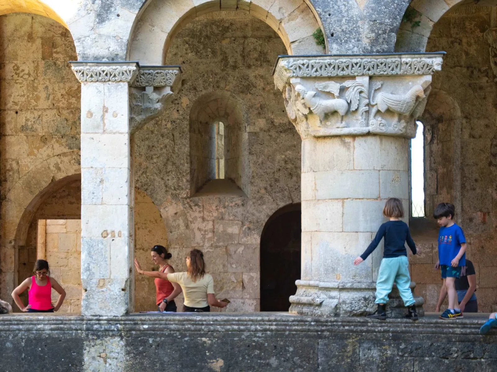 Children playing among the Romanesque ruins of La Sauve-Majeure Abbey in Bordeaux, featuring stone columns and medieval archways.