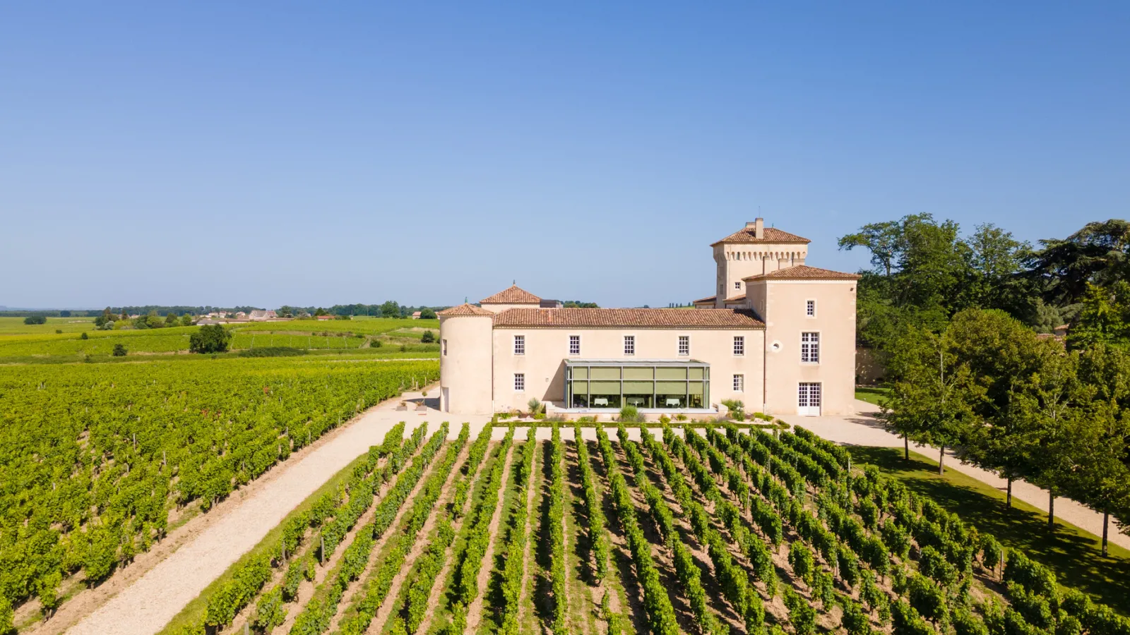 Lafaurie-Peyraguey Castle, a white Aquitanian-style building with towers and tiled roofs, surrounded by orderly vineyard rows in the Bordeaux region.