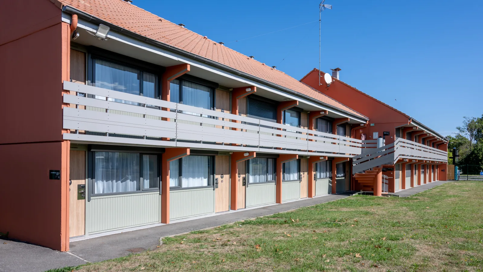Campanile Nature Bordeaux Sud hotel in Gradignan, modern multi-story building with orange and white facade, balconies, large windows and tiled roof, surrounded by green landscape.