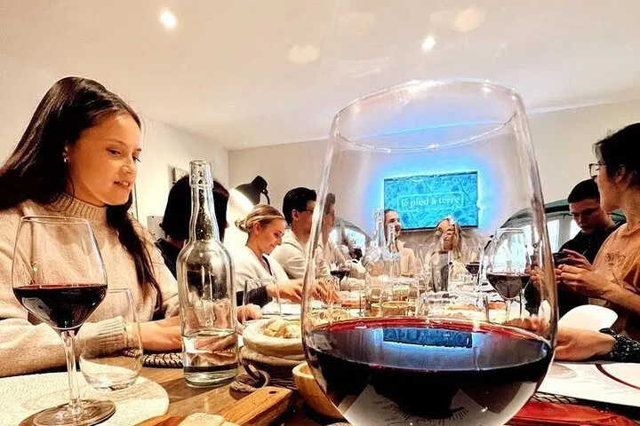Wine tasting in Bordeaux: a woman holding a glass of red wine in front of a large decanter, surrounded by guests at a restaurant table.