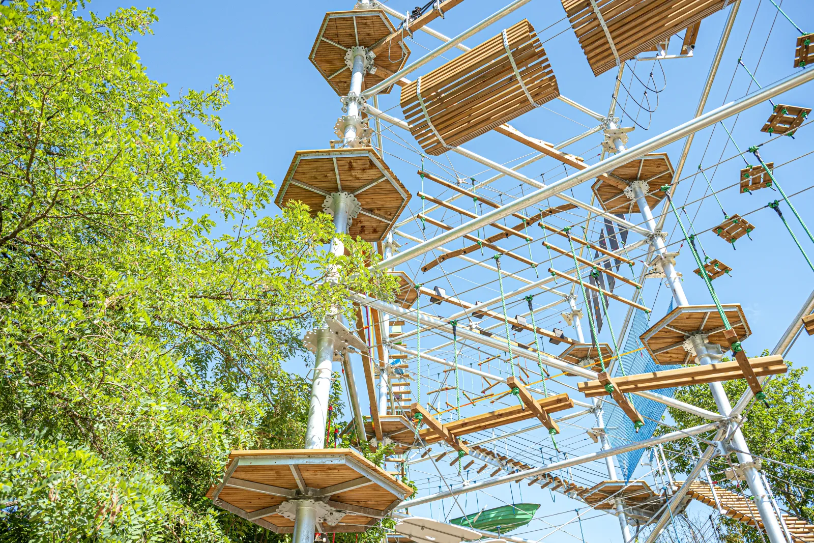 The Cimes of Bordeaux Pessac, an aerial adventure park with ziplines, suspended bridges and rope nets woven between trees against a blue sky.