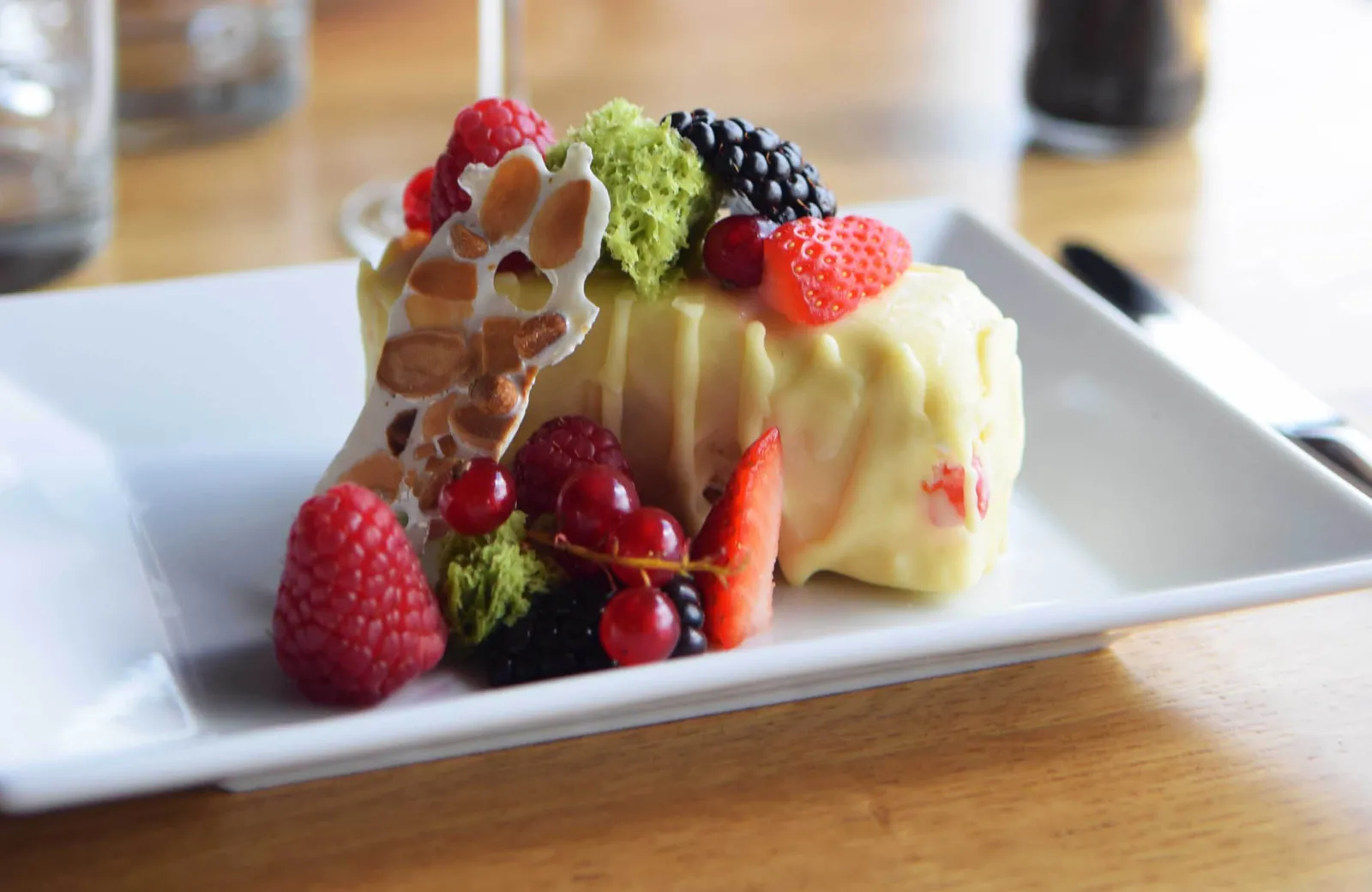 Slice of cake with pastry cream topped with fresh red and black berries and sliced almonds on a white plate