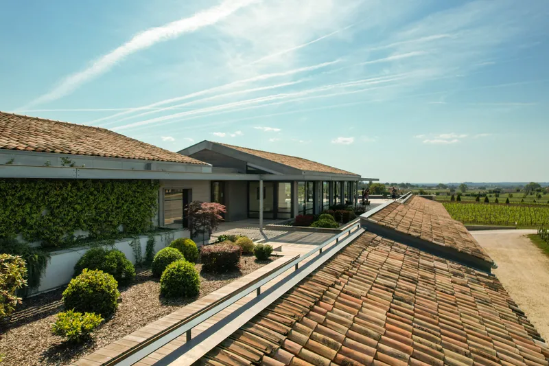 Aerial view of Château Balestard La Tonnelle near Bordeaux, featuring modern architecture with traditional tile roofs, surrounded by vineyards and landscaped gardens.