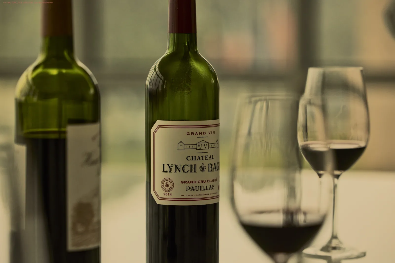 Bottle of Château Lynch-Bages, Grand Cru Classé Pauillac 2014, surrounded by other wine bottles and glasses filled with red wine in a tasting setting.