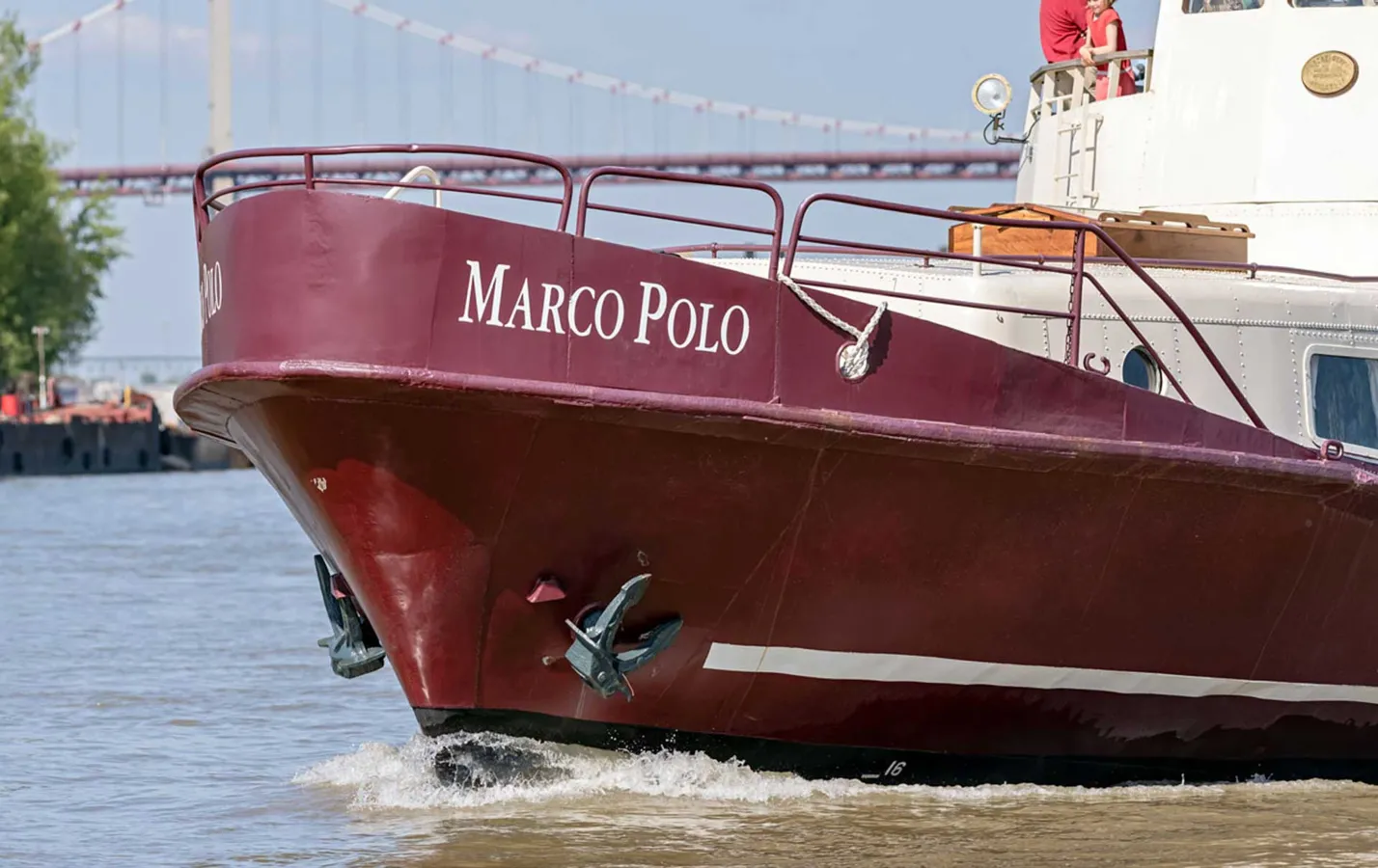 The Marco Polo ship, painted in dark burgundy, partially beached with the Pont de Pierre bridge visible in the background at Bordeaux.