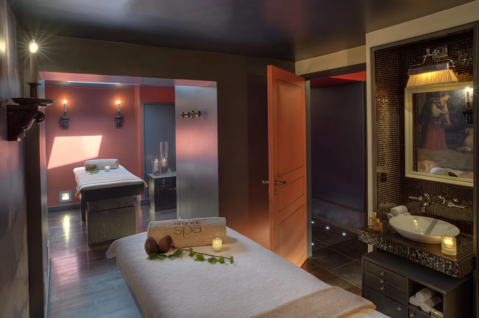Luxury interior of Guerlain Spa in Bordeaux featuring a treatment room with white massage table, soft pink ambient lighting, bathing basin, illuminated mirrors, and elegant decor